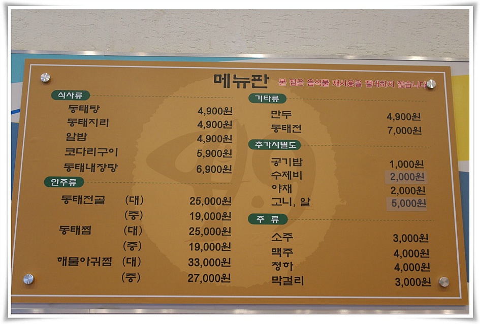 벽면에 걸려 있는 메뉴판, 식사류:동태탕 4900, 동태지리 4900, 알밥 4900, 코다리구이 5900, 동태내장탕 6900, 안주류:동태전골 25000(대), 19000(중), 동태찜 25000(대), 19000(중), 해물아귀찜 33000(대), 27000(중), 기타류:만두 4900, 동태전 7000, 추가시별도:공기밥 1000, 수제비 2000, 야채 2000, 고니 알 5000, 주류:소주 3000, 맥주 4000, 청하 4000, 막걸리 3000